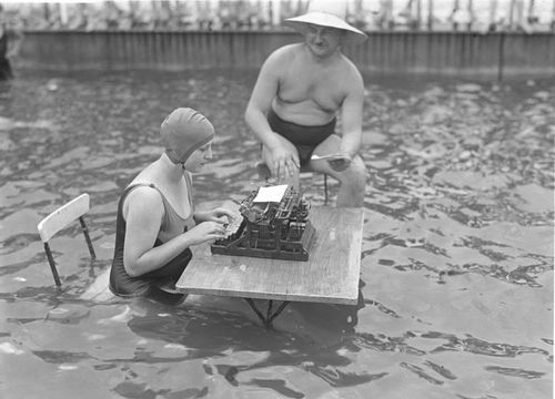 Old photo of a woman using a typewriter while in a swimming pool